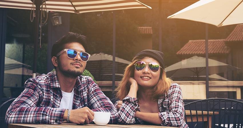 兩個學生戴著太陽鏡，在外部露台上喝咖啡。
